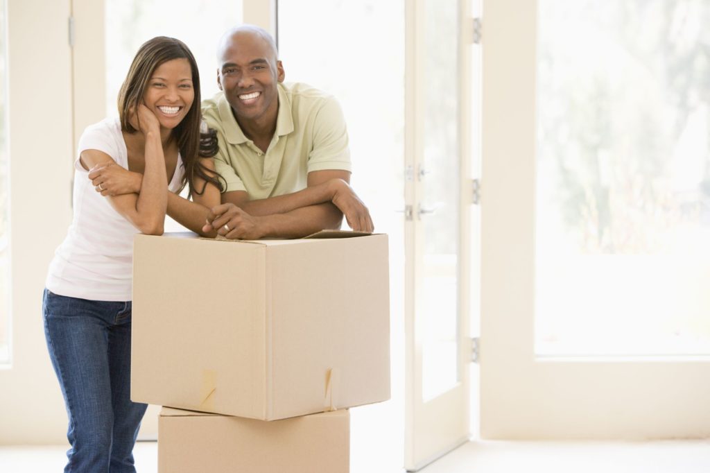 alt-text= "a happy couple who budgeted closing costs into their home sale unpack a box at their new home"