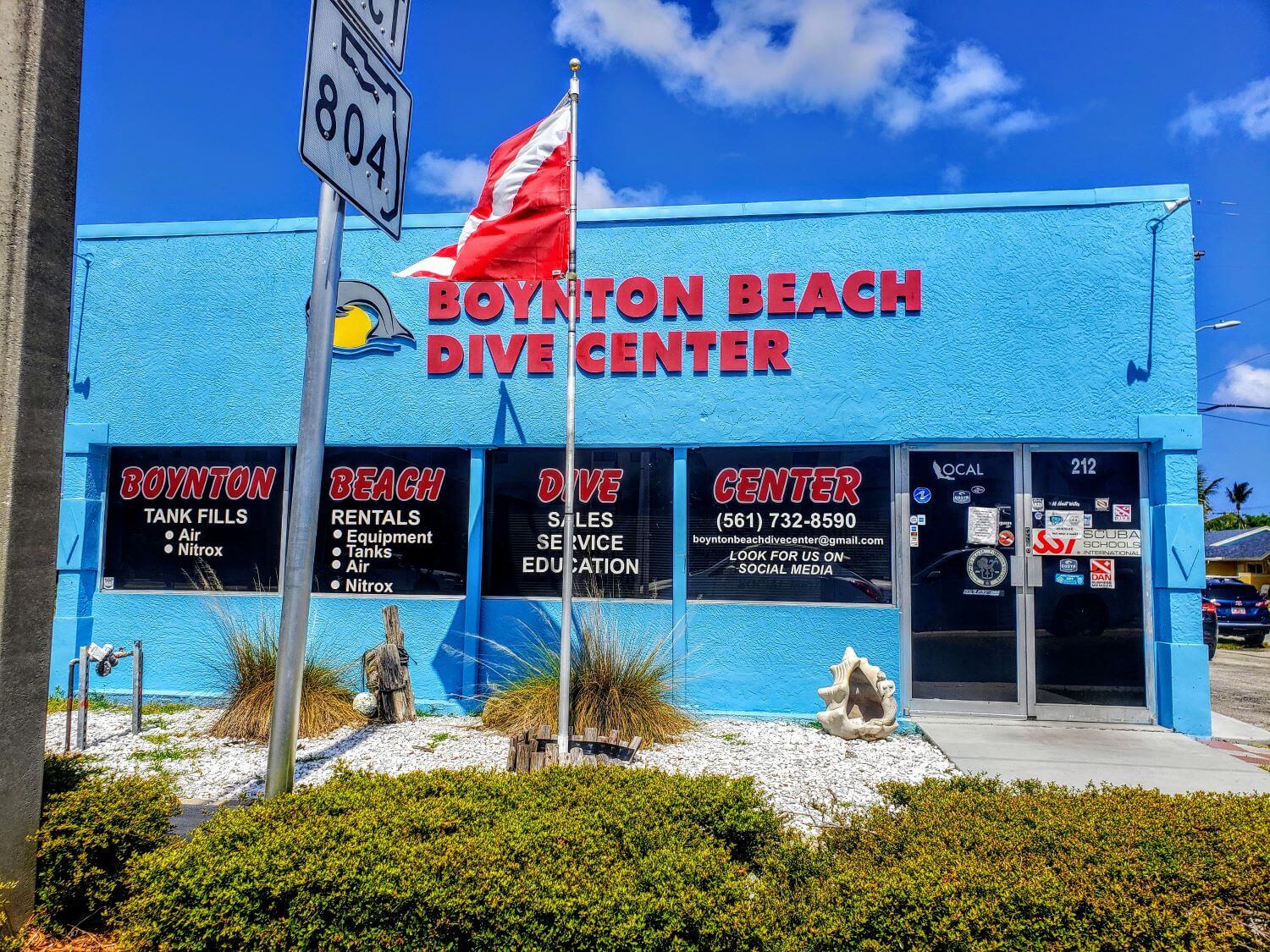 alt text = "dive flag flying with blue building behind reading boynton beach dive center"