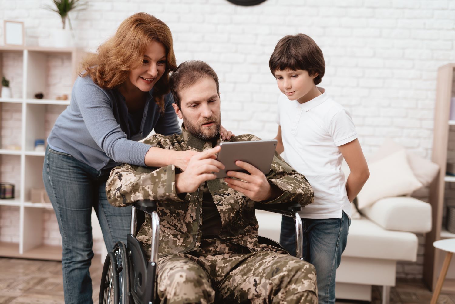 Uniformed disabled veteran in a wheelchair browsing florida homes on a tablet with wife and son