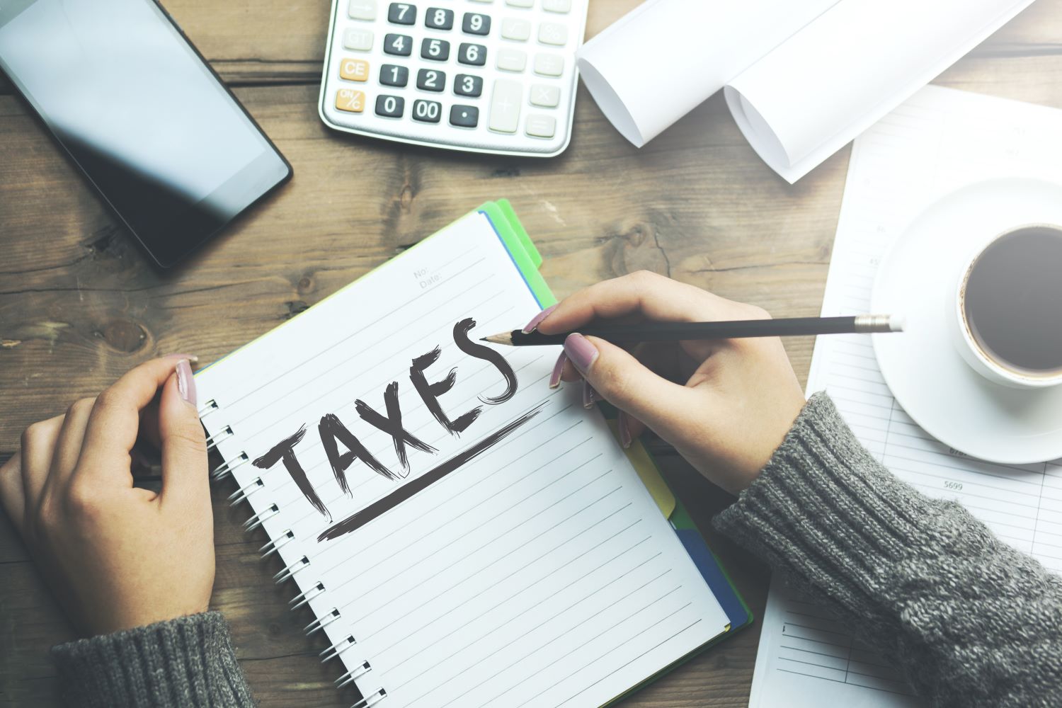 Woman's hands, one with a pencil, around a notebook that reads TAXES